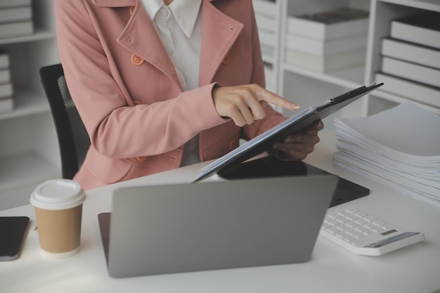 Attraktive lächelnde junge asiatische Geschäftsfrau, die zu Hause im Büro arbeitet Asiatische Frau, die an einem Laptop-Computer mit Tablet arbeitet