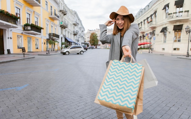 Attraktive, lustige Shopaholic-Frau im Herbstmantel und Hut, die viele Papiereinkaufstüten in der europäischen Stadt hält