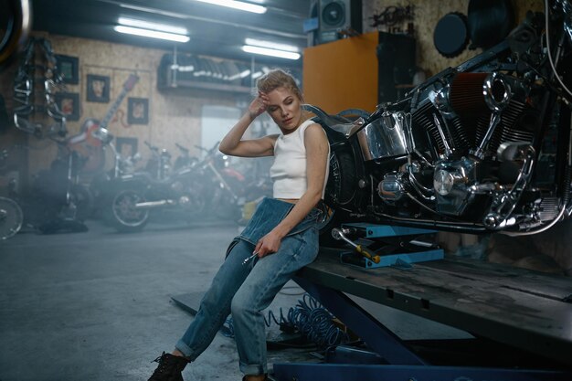 Attraktive Mechanikerin posiert vor der Kamera in der Motorradwerkstatt. Professionelle Reparaturfrau in authentischer Werkstatt