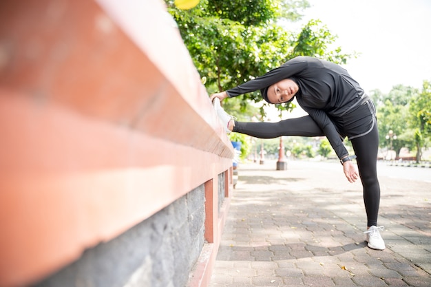 Attraktive muslimische Asiatin streckt ihr Bein während der Sportzeit im Freien an sonnigen Tagen