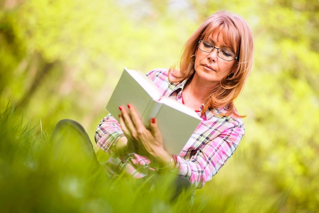 Attraktive reife Frau, die ein Buch im Park liest