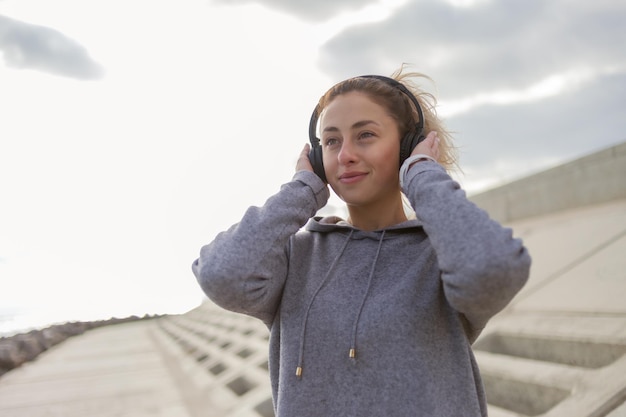 Attraktive schlanke Frau in Sportbekleidung hört Musik über Kopfhörer im Freien
