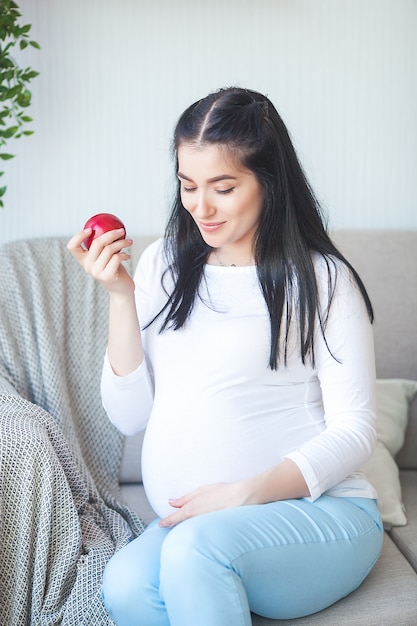 Attraktive schwangere Frau mit Apfel. Erwartung der Frau, die gesundes Lebensmittel hält. Dame, die einen roten Apfel isst. Richtige Ernährung für die Schwangerschaft.