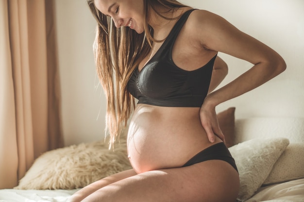 Attraktive schwangere Frau sitzt im Bett und hält ihren Bauch