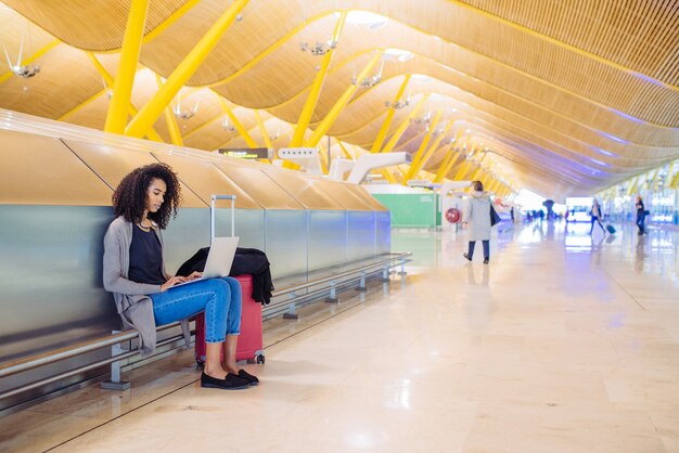 Attraktive schwarze Frau am Flughafen, der mit Laptop sitzt und arbeitet