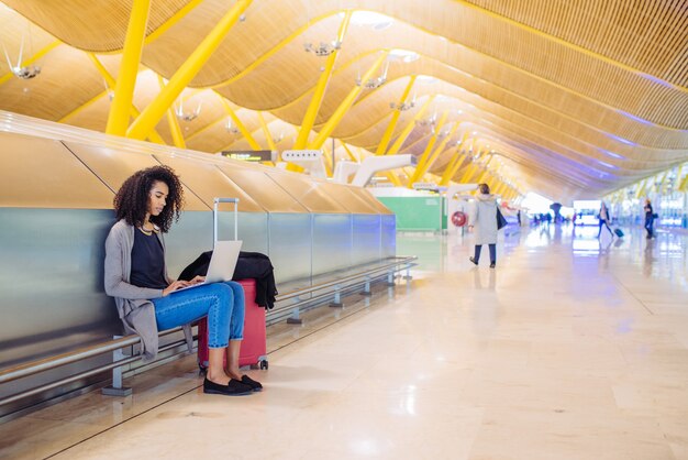 Foto attraktive schwarze frau am flughafen, der mit laptop sitzt und arbeitet