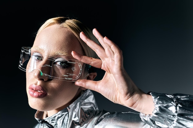 Attraktive seltsame Frau in Science-Fiction-Brille und silberner Kleidung, die auf dunkler Kulisse in die Kamera schaut