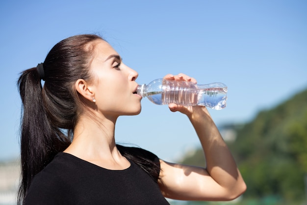 Attraktive sportliche Frau trinkt Wasser beim Laufen im Park am sonnigen Morgen. Platz für Text