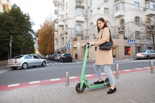 Attraktive stilvolle Frau, die auf dem Bürgersteig in der Stadt Elektroroller fährt, Kopierraum