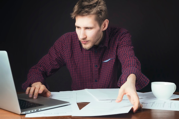 Attraktive Studentenarbeit mit Papier und Laptop und Kaffeetrinken auf dunklem Hintergrund b