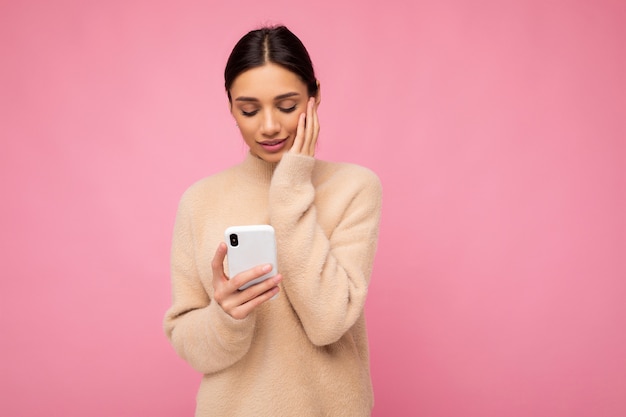 Attraktive süße junge Brunetfrau, die beige warmen Pullover stehend trägt