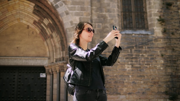 Attraktive Touristenfrau, die ein Selfie macht, verwendet ein Smartfone, während sie auf der Straße geht. Freiheit genießen. Sie lächelt und genießt den Spaziergang.