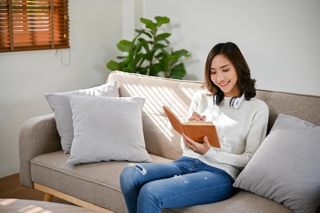 Attraktive und glückliche asiatische Frau liest gerne ein Buch, während sie sich in ihrem Wohnzimmer ausruht