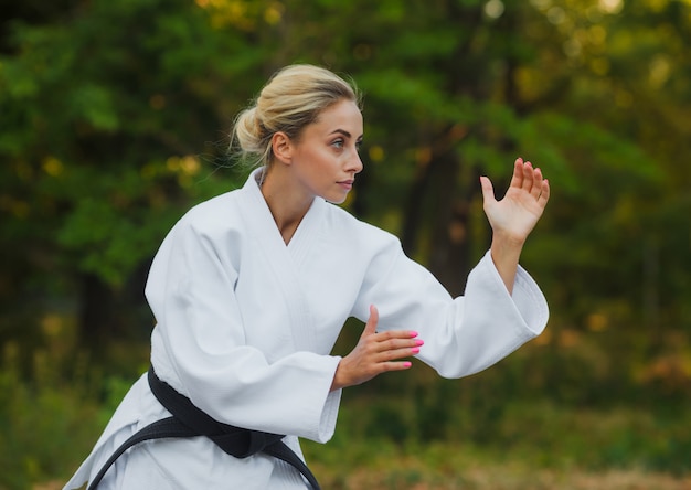 Attraktive weibliche Meisterkämpferin in einem weißen Kimono mit einem schwarzen Gürtel steht in einer Kampfhaltung im Freien