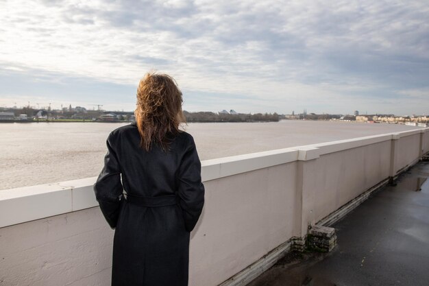 Attraktive Winterfrau im Regenmantel Tourist genießt den Blick auf den Fluss garonne in der Bordeaux-Stadt Gironde