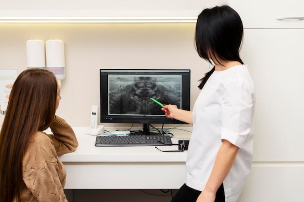 Attraktive Zahnärztin spricht mit der Patientin zeigt ein Foto ihrer Zähne auf dem Monitor das Problem, das gelöst und der Zahn geheilt werden muss Moderne Technologien in der Zahnbehandlung