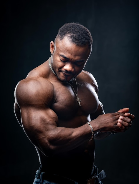Attraktiver afrikanischer männlicher Boxer, der mit nacktem Oberkörper aufwirft. Dunkler Hintergrund. Fitness-Mann unter zurückhaltender Beleuchtung.