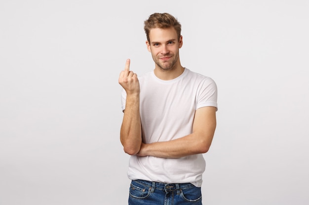 Attraktiver blonder bärtiger Mann im weißen T-Shirt, das Mittelfinger zeigt