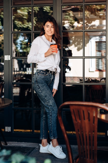 Attraktiver Brunette, der mit einem Tasse Kaffee in ihren Händen in einem Café aufwirft.