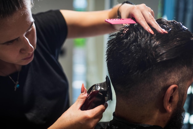 Attraktiver Friseur, der einen Haarschnitt eines hübschen Hipsters in Friseursalon-Friseurwerkzeugen macht