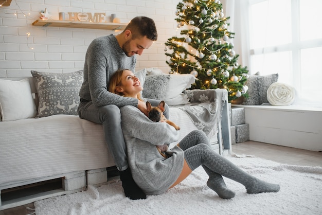 Attraktiver fröhlicher Mann und Frau sitzen nahe Weihnachtsbaumumarmung