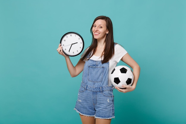 Attraktiver Fußballfan der jungen Frau jubelt auf, unterstützt Lieblingsmannschaft mit Fußball, runde Uhr einzeln auf blautürkisem Wandhintergrund. Menschen Emotionen, Sport Familie Freizeit Lifestyle-Konzept.