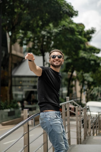 Attraktiver glücklicher tätowierter Mann, der auf der Straße in Kuala Lumpur lächelt. Urbane Männer, Kleidungsstil. Seifenblasen fliegen in die Luft.