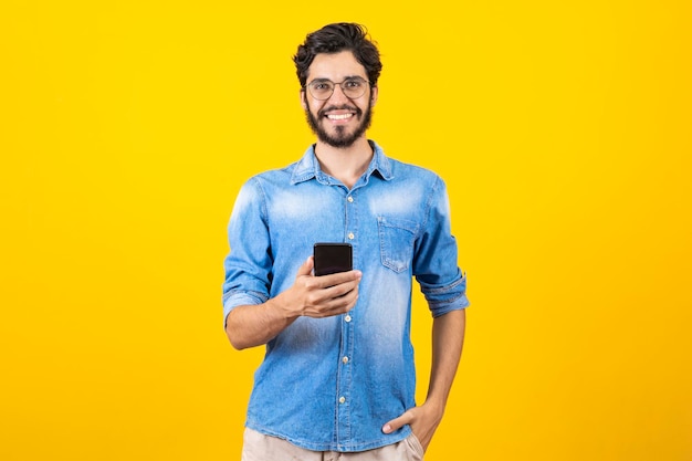 Attraktiver gutaussehender junger Mann mit Brille, der mit einem Handy per SMS auf isoliertem Hintergrund chattet