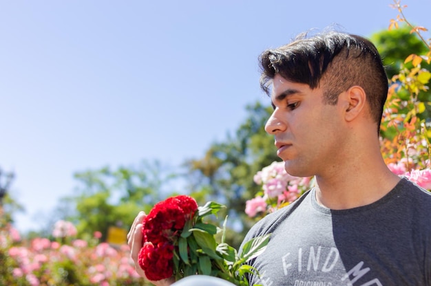 Attraktiver hispanischer Latino-kaukasischer Mann im Freien in einem Park mit einem Garten, der wahnsinnig verliebt ist und einen Blumenstrauß ansieht und an seine geliebte Freundin denkt