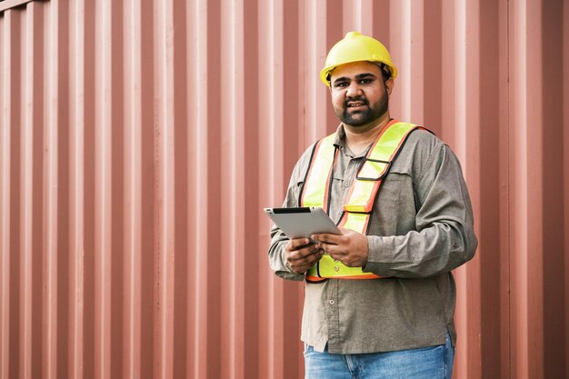 Foto attraktiver indischer männlicher industrieingenieur in gelber sicherheitsweste mit verschwommenem behälter