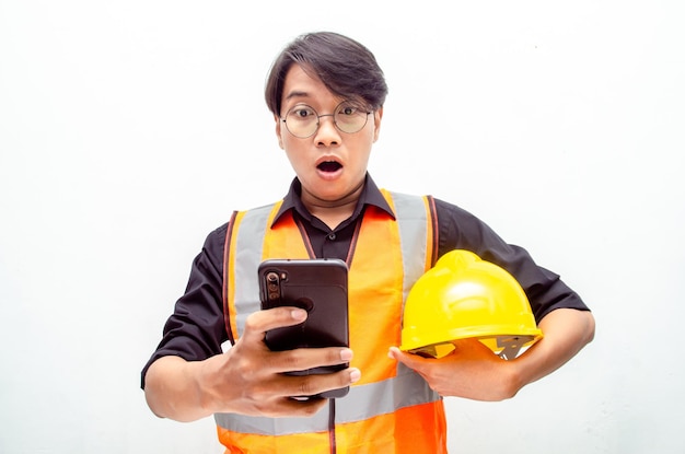 attraktiver junger asiatischer männlicher bauarbeiter im schutzhelm und in der weste, die telefon halten