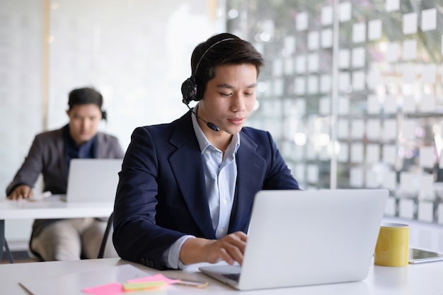 Attraktiver junger asiatischer männlicher Callcenter-Agent im Headset-Beratungskunden.