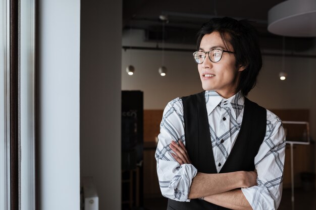 Attraktiver junger asiatischer Mann, der Fenster betrachtet.