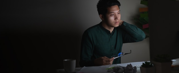 Attraktiver junger asiatischer Mann, der spät nachts Laptop betrachtend arbeitet