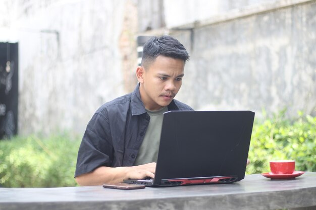 Attraktiver junger asiatischer Mann mit Laptop im Coworking Space mit fröhlichem Gesicht