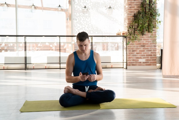 Attraktiver junger erwachsener Mann, der Yoga und Meditation online mit dem Smartphone praktiziert