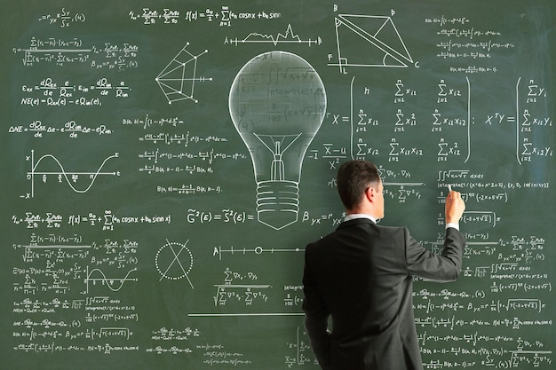 Attraktiver junger europäischer Geschäftsmann, der abstrakte Lampenskizze mit mathematischen Formeln auf Tafelwandhintergrund zeichnet Intelligenzidee Lösung Wissenschafts- und Innovationskonzept