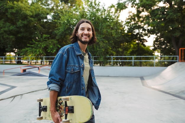 Attraktiver junger Hipster-Mann, der mit einem Skateboard im Skatepark steht