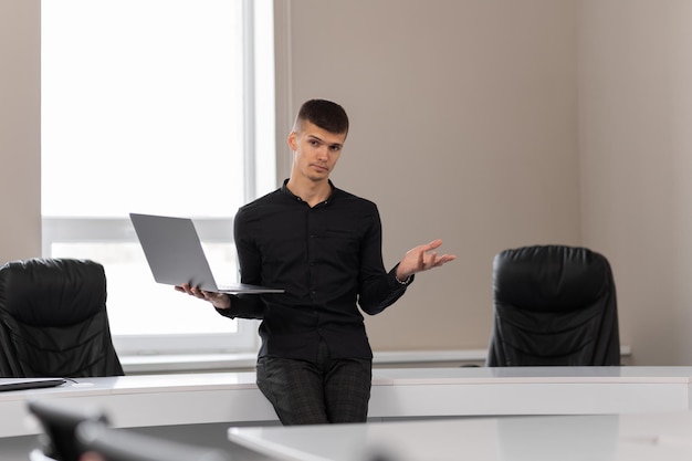 Attraktiver junger Mann im Büro in einem Konferenzraum, der einen Laptop in seinen Händen hält