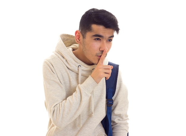 Attraktiver junger Mann mit dunklem Haar in weißem Kapuzenpulli mit blauem Rucksack, der im Studio Shhhh zeigt