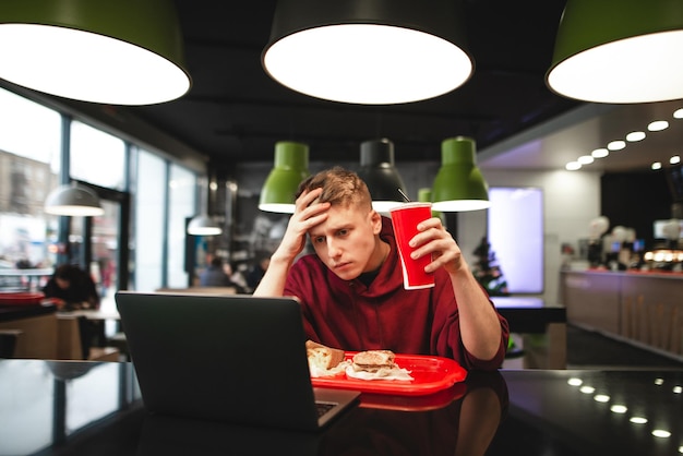 Attraktiver junger Mann serviert Fast Food in einem Restaurant und benutzt einen Laptop