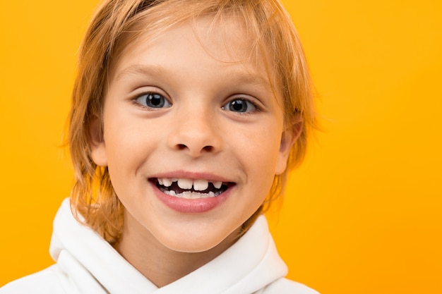 Attraktiver lächelnder blonder Junge in einem weißen Hoodie auf einer gelben Nahaufnahme