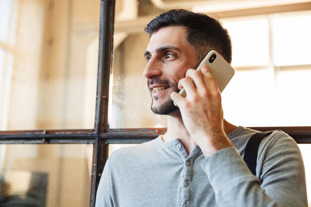 Attraktiver lächelnder junger Mann, der in der Nabe steht und mit dem Handy spricht