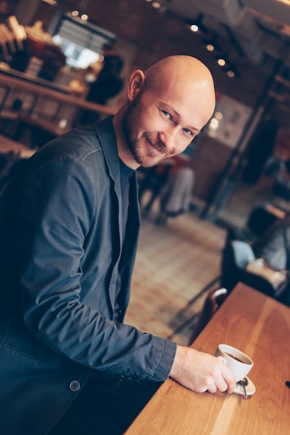 Attraktiver lächelnder kahler Mann mit dem Kaffee, der Kamera im Café betrachtet