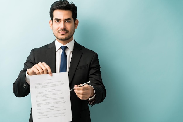 Attraktiver lateinischer männlicher Unternehmer, der Stift und Vereinbarung gegen blauen Hintergrund anbietet