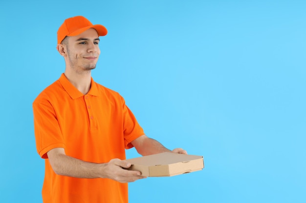 Attraktiver Lieferbote mit Pizzakarton auf blauem Hintergrund