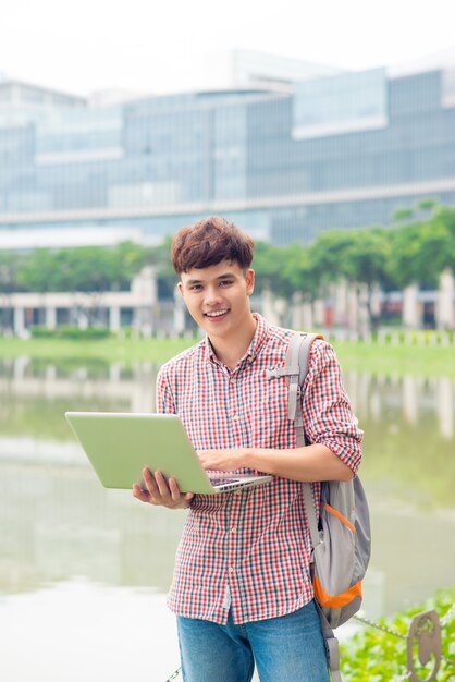 Attraktiver männlicher asiatischer Student benutzt Laptop auf dem Campus