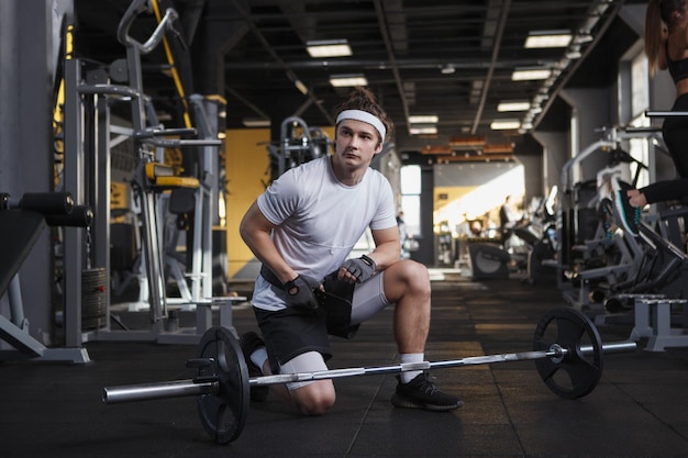 Attraktiver männlicher Gewichtheber, der vor dem Langhanteltraining einen Trainingsgürtel anlegt