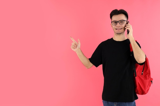 Attraktiver männlicher Student, der am Telefon gegen rosa Hintergrund spricht