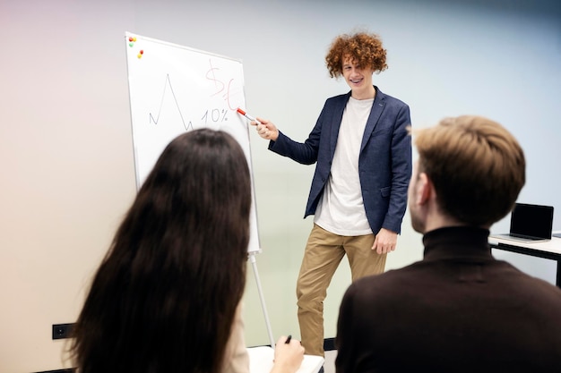 Foto attraktiver mann, der auf ein auf flipchart gezeichnetes diagramm zeigt junger lehrer hält vorlesungen für studenten